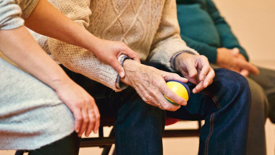 A carer supports an older person with a gentle hand exercise